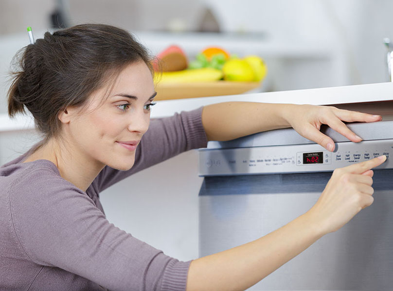 A happy woman setting the time delay on her dishwasher