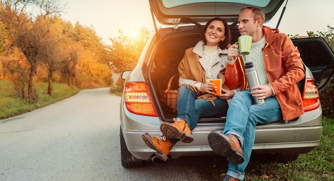 Two people enjoying coffee from the back of their car